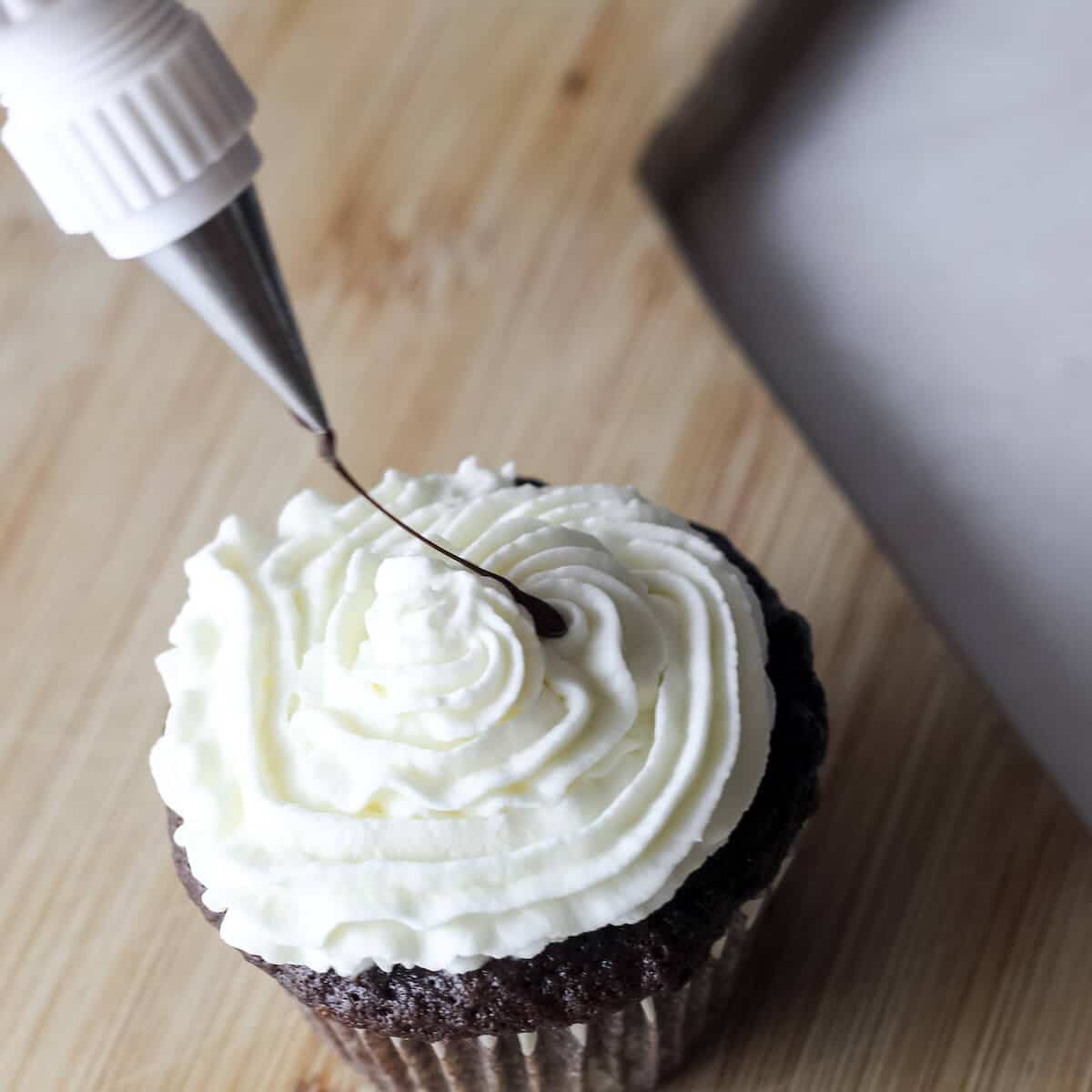 frosting with marshmallow frosting on top, ganache is being drizzled on top.