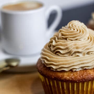 Vanilla cupcake topped with espresso buttercream frosting. An espresso cup with espresso in the background.
