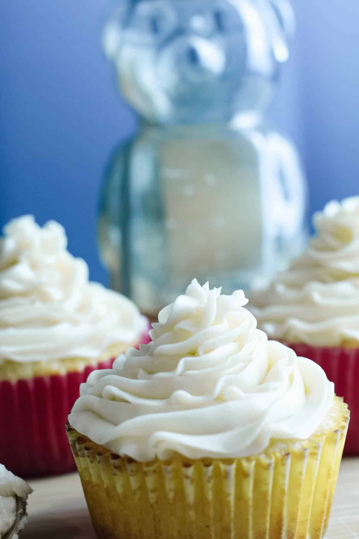 3 cupcakes with honey buttercream icing and a jar of honey shaped like a bear in the background.