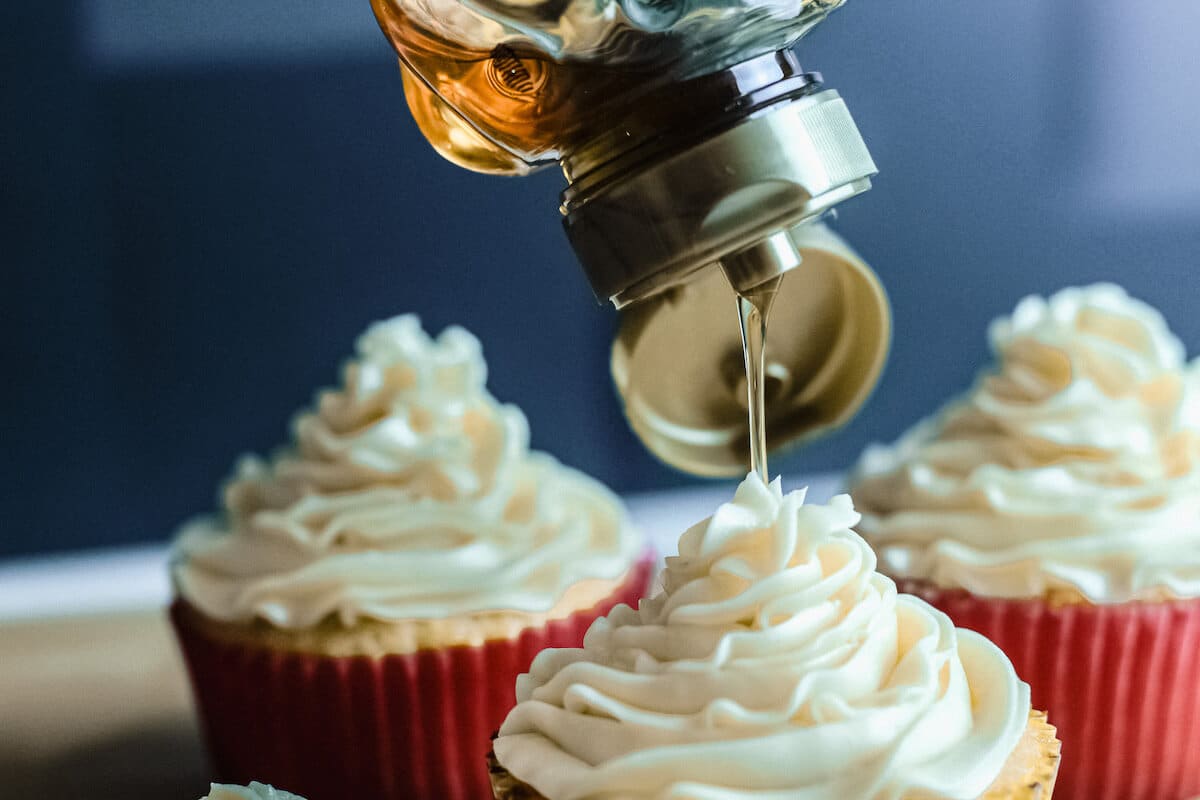 3 cupcakes with honey buttercream. Honey is drizzled on top of the front cupcake. 